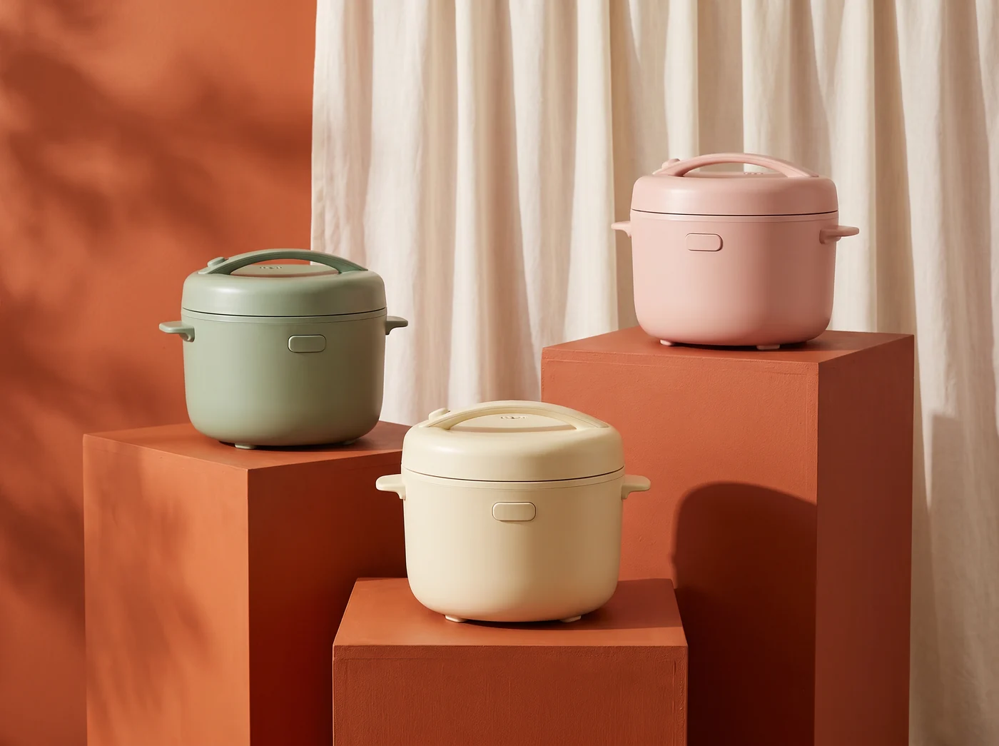 Three retro rice cookers in sage, cream and blush on painted plinths