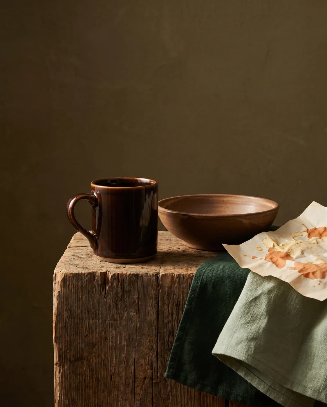 A dark glazed ceramic cup and bowl on a wooden block