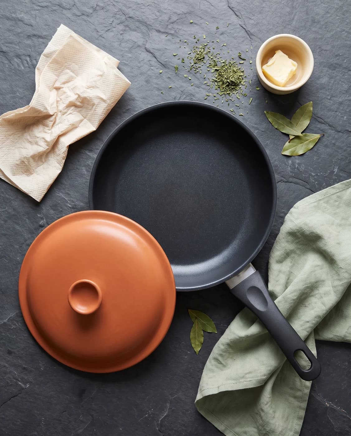 A charcoal non-stick frying pan with a terracotta lid on slate