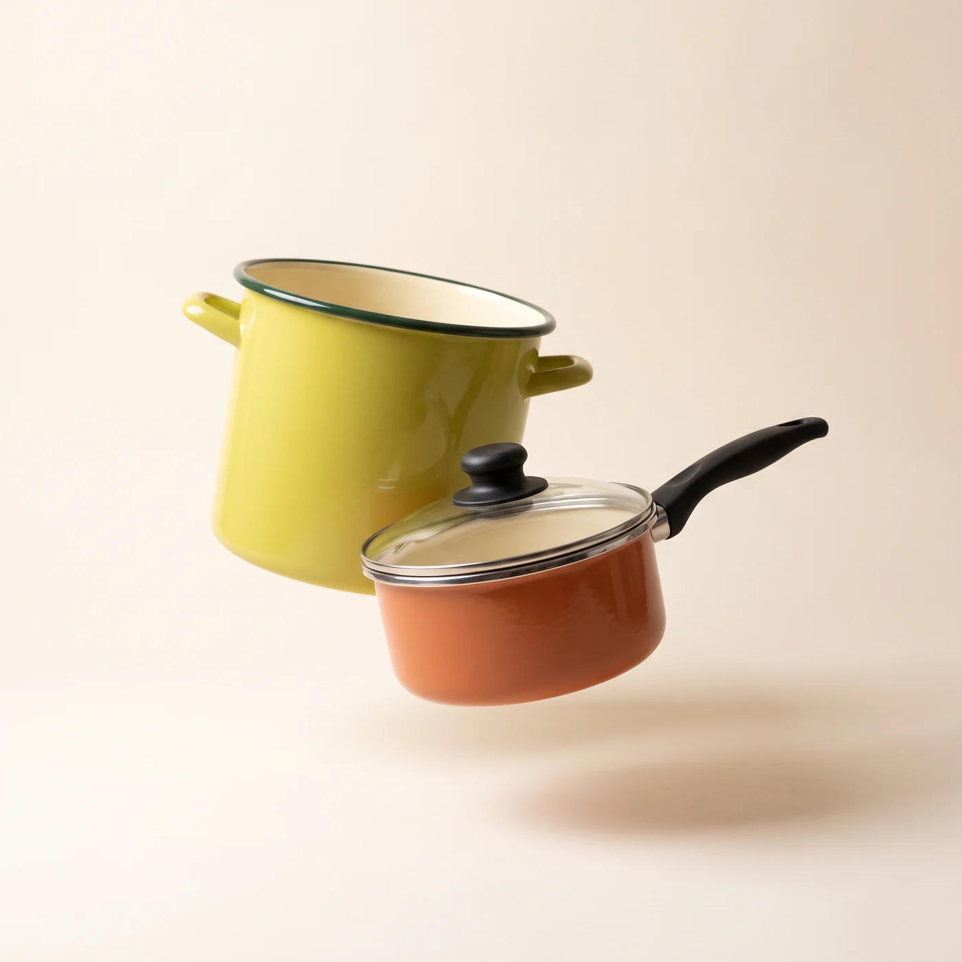 A chartreuse enamel stockpot beside a terracotta saucepan with a glass lid