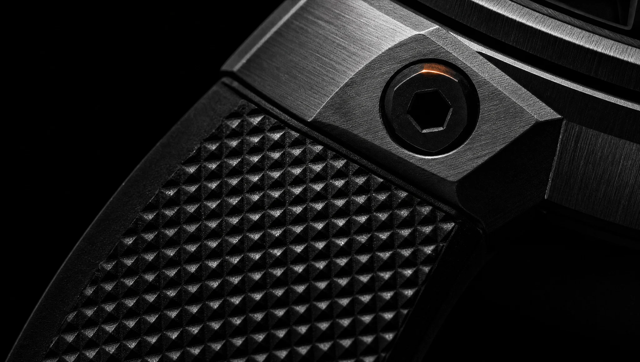Macro of the strap, lug and hex bolt in near-monochrome, a single ember glint on the bolt head.