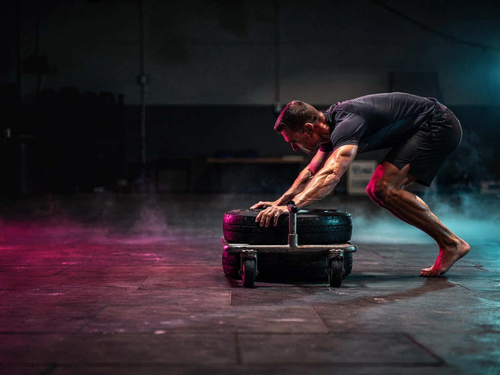 An athlete driving a sled across a dark floor in cold light