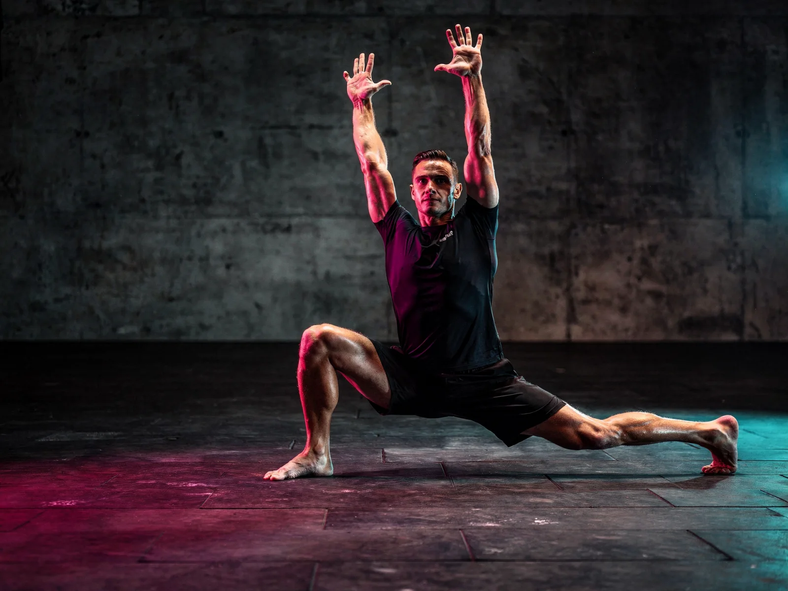 An athlete in a deep lunge on a dark floor, lit magenta and cyan
